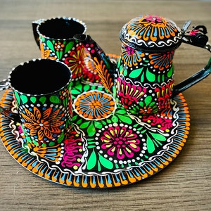 Può includere: Un set da tè in metallo nero con motivi floreali colorati. Il set comprende una teiera, due tazze e un vassoio.