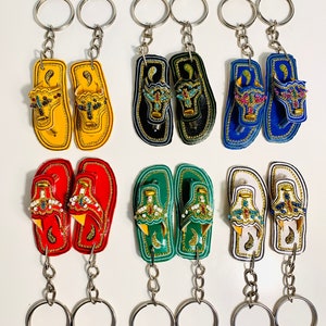 May include: Six pairs of colorful leather flip-flop keychains with intricate designs and beaded accents. The keychains are attached to silver key rings.
