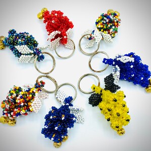 May include: A set of seven colorful beaded keychains, each featuring a different color combination and design. The keychains are made of small beads and have a ring attached to the top for attaching keys.