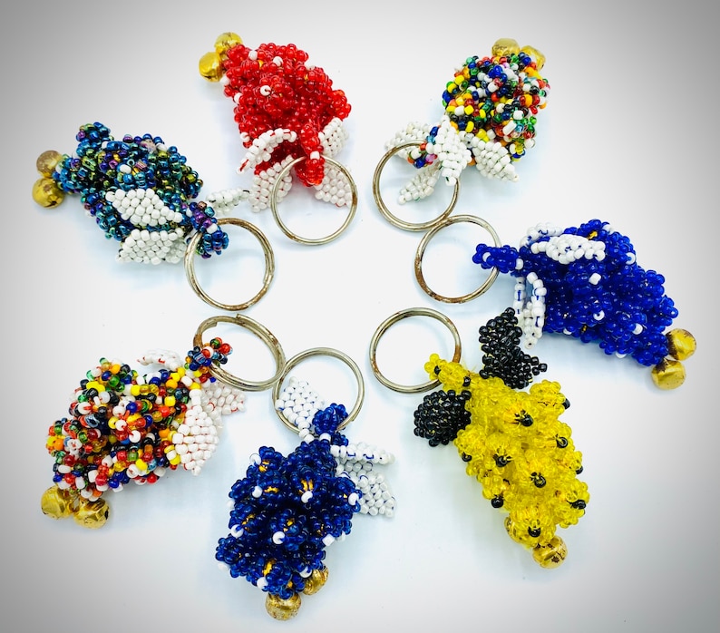 May include: A set of seven colorful beaded keychains, each featuring a different color combination and design. The keychains are made of small beads and have a ring attached to the top for attaching keys.
