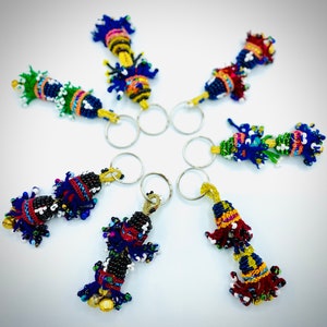 May include: Seven colorful beaded keychains with silver key rings. Each keychain features a different design with a variety of colors, including blue, green, red, yellow, and white.