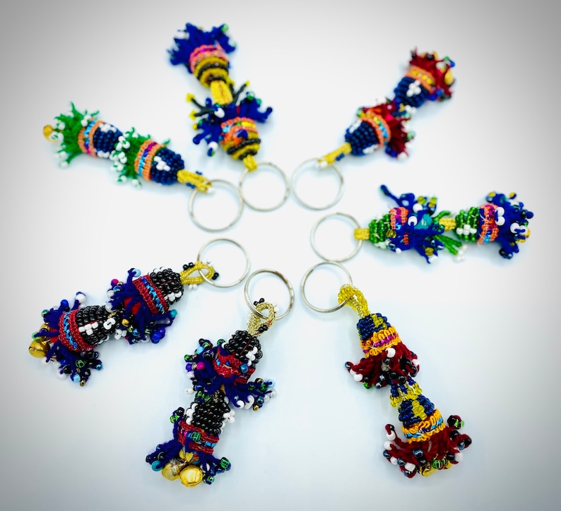 May include: Seven colorful beaded keychains with silver key rings. Each keychain features a different design with a variety of colors, including blue, green, red, yellow, and white.