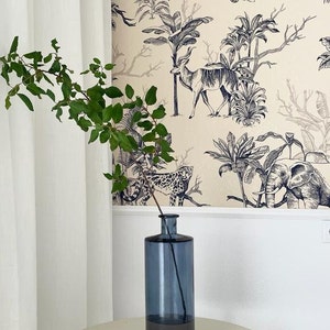 May include: A tall, cylindrical, translucent blue glass vase with a narrow neck. A single slender branch with small green leaves is placed inside the vase, extending upwards from the opening. The vase has a smooth, uniform surface.