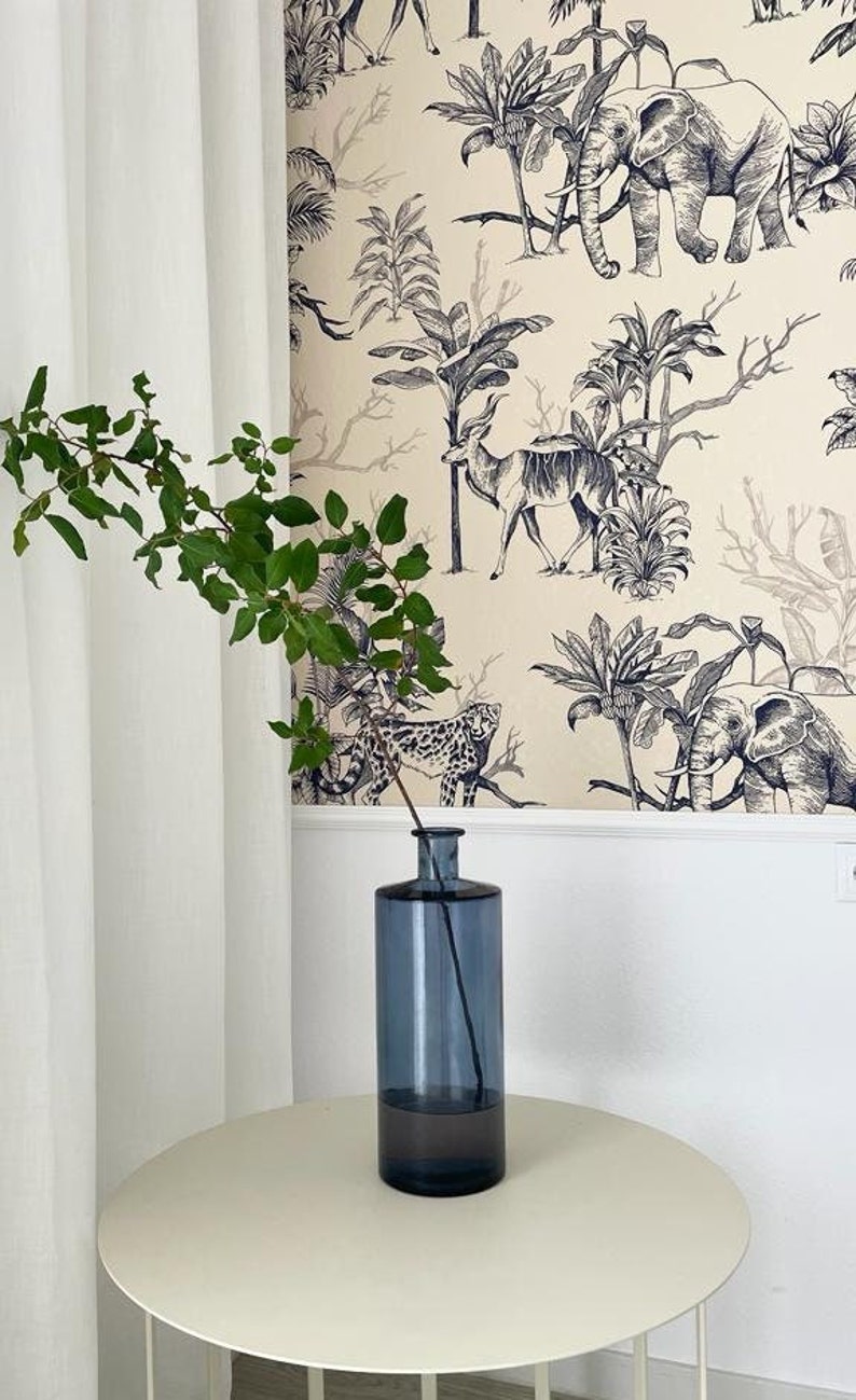 May include: A tall, cylindrical, translucent blue glass vase with a narrow neck. A single slender branch with small green leaves is placed inside the vase, extending upwards from the opening. The vase has a smooth, uniform surface.