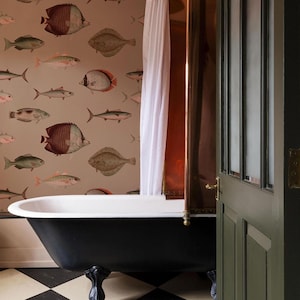 May include: A black clawfoot bathtub sits in a bathroom with a beige wall covered in a wallpaper pattern of colorful fish. A white shower curtain hangs in the background.