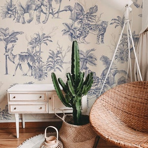 May include: A room interior featuring wallpaper with a blue ink-style jungle animal print, a white wooden cabinet, a tall green cactus in a woven basket, a round white rug, a small wooden lantern, and a round woven wicker chair with metal legs.