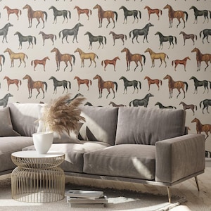 May include: A light gray sofa with a white round wire-frame side table and a white vase containing dried pampas grass. The wall behind features wallpaper with a repeating pattern of brown and black horses on a light beige background.