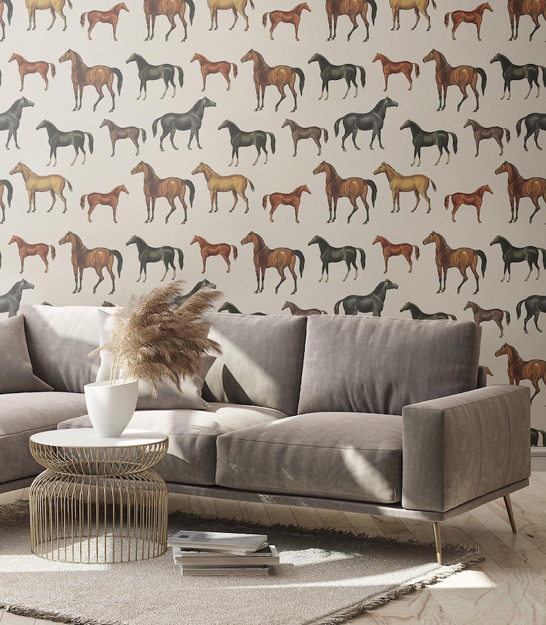 May include: A light gray sofa with a white round wire-frame side table and a white vase containing dried pampas grass. The wall behind features wallpaper with a repeating pattern of brown and black horses on a light beige background.