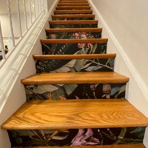 May include: A set of wooden stairs with a black and green floral wallpaper design on the risers. The wallpaper features large leaves, flowers, and stems.