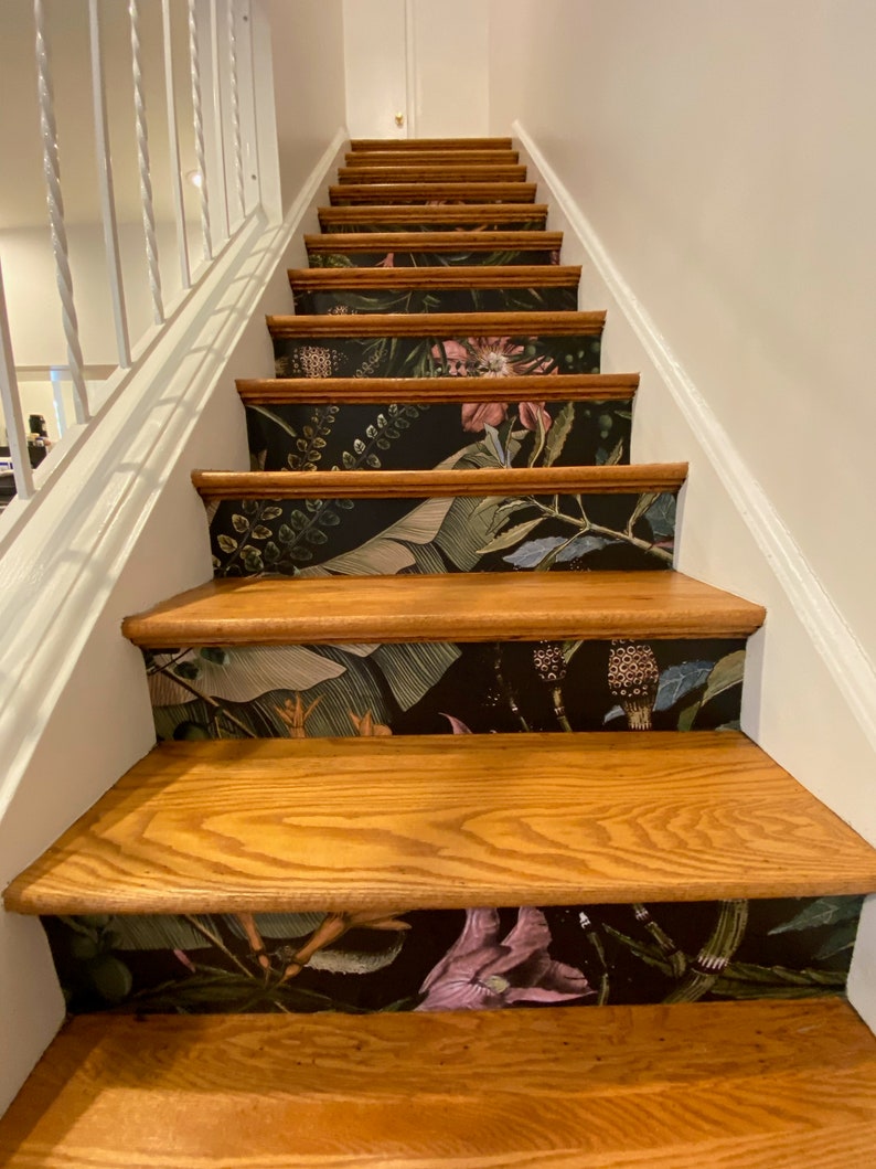 May include: A set of wooden stairs with a black and green floral wallpaper design on the risers. The wallpaper features large leaves, flowers, and stems.