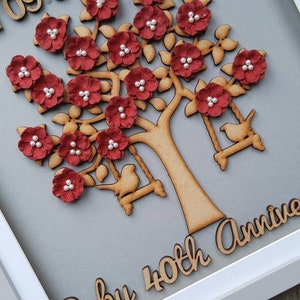 Könnte beinhalten: Ein gerahmter Holzbaum mit roten Blüten und weißen Perlenakzenten. Der Baum hat zwei hölzerne Vögel auf Schaukeln. Das Datum "09.05.1981" und das Wort "DAD" sind auf dem Rahmen abgebildet. Die Worte "Ruby 40th Anniv" sind unten auf dem Rahmen abgebildet.