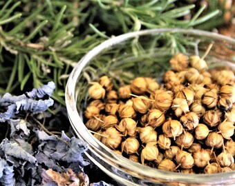 May include: A glass bowl filled with dried coriander seeds, surrounded by sprigs of rosemary and dried lavender flowers.
