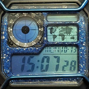 May include: A digital watch with a blue and black design. The watch face displays the time, date, and a world map. The watch also features a compass-like dial and a blue glittery bezel.