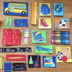 May include: A collection of colourful felt squares with various school-themed images, including a school bus, crayons, a globe, a backpack, a laptop, a pencil, a microscope, a milk carton, and a skateboard. The squares also feature letters of the alphabet, constellations, and the words "English", "Maths", and "Science".