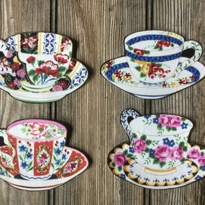 May include: Four decorative teacups and saucers with floral patterns. The teacups are white with colorful floral designs and gold accents. The saucers are white with matching floral designs.