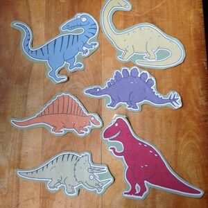 May include: Six colorful paper cutouts of different dinosaurs, including a blue stegosaurus, a yellow brachiosaurus, a purple spinosaurus, an orange spinosaurus, a green triceratops, and a red tyrannosaurus rex.