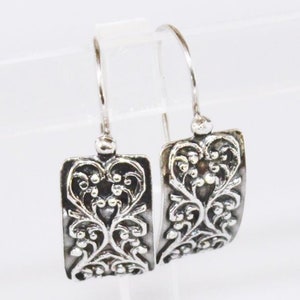 Puede incluir: Un par de pendientes de plata con un diseño rectangular que presenta intrincados patrones florales.