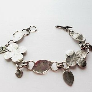 May include: Silver bracelet with a floral design. The bracelet features several flower-shaped charms and a leaf charm. The bracelet has a toggle clasp.