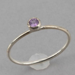 May include: A delicate silver ring with a small, round, purple amethyst gemstone.