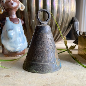 Op de afbeelding: Een vintage bronzen bel met een lusvormige handgreep. De bel heeft een uitlopende vorm en is versierd met een geëtst bladerpatroon. De bel is verouderd met patina en blauwgroene oxidatie.