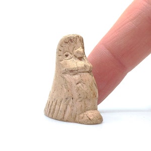 Op de afbeelding: Een klein, handgesneden, beige keramiek beeldje van een vogel met een gedetailleerd gezicht en een textuur.