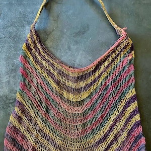 May include: A colourful, hand-woven net bag with a long strap. The bag features a striped pattern in shades of yellow, pink, purple, green, and brown. The strap is a twisted, rope-like material.