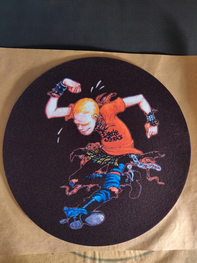 May include: A black felt turntable slipmat with a cartoon illustration of a person wearing a red shirt with the text "Circle Jerks" printed on it. The person is wearing blue jeans, black boots, and a chain around their waist.