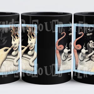 May include: Black ceramic coffee mug featuring a graphic of the album cover for "Strange Times" by The Chameleons. The album cover depicts a surreal illustration of a person with a long, thin nose and a hand reaching out to touch their nose.
