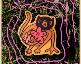 May include: A sticker featuring a cartoon cat-like creature with a black mask and holding pink flowers. The sticker has an orange and yellow color scheme, with a pink outline. The sticker is placed on a bed of green grass.