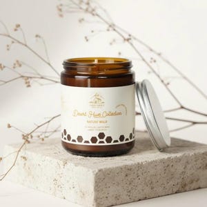 May include: A brown glass jar candle from the Desert Hive Collection, labeled "Nature Walk." The label features a mountain graphic and honeycomb design. The silver lid is off to the side. The candle sits on a gray stone surface.