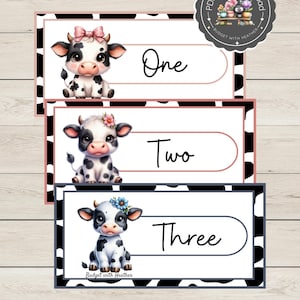 May include: Three printable cards featuring adorable cartoon cows with floral accents. Each card displays a number: One, Two, and Three, with a corresponding cow illustration. The cards have a black and white cow print border and are labeled "Budget with Heather."