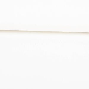 Pode incluir: Um close-up de tecido branco com uma textura sutil. O tecido está dobrado, criando uma linha horizontal na imagem. A iluminação é suave, destacando a textura e a cor esbranquiçada do material.