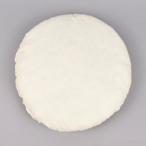 May include: A round, white, cotton cushion with a simple design.
