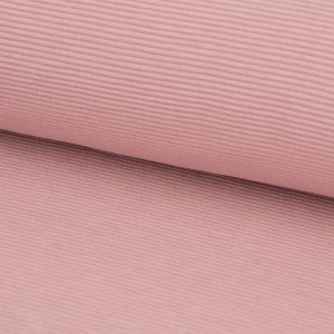 Könnte beinhalten: Nahaufnahme eines weichen, rosa gerippten Stoffes. Der Stoff hat eine subtile Textur und eine glatte, gleichmäßige Oberfläche.