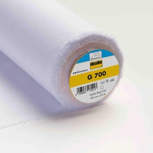 Peut inclure: Un rouleau de tissu thermocollant blanc Vlieseline G 700. L'étiquette circulaire à l'extrémité du rouleau affiche le nom de la marque, le numéro de modèle G 700, un code-barres, le texte 100% BW/CO, 90 cm x 25 m et des symboles d'entretien.
