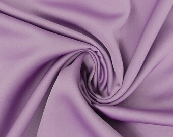 Può includere: Un primo piano di un tessuto morbido e liscio di colore lilla, con un drappeggio delicato. Il tessuto è piegato e attorcigliato, creando una texture morbida e fluida.