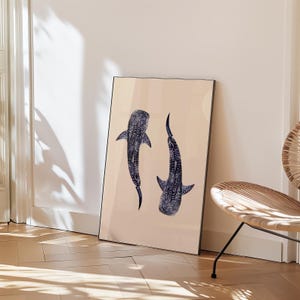 K&ouml;nnte beinhalten: Ein gerahmter Kunstdruck mit zwei stilisierten Walhaien in Marineblau mit wei&szlig;en Punkten auf beigem Hintergrund. Das Kunstwerk wird auf einem Holzboden pr&auml;sentiert und lehnt an einer Wand.