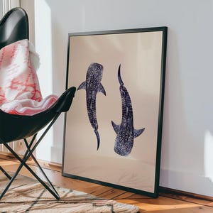 K&ouml;nnte beinhalten: Gerahmter Kunstdruck mit zwei stilisierten Walhaien in Blau- und Wei&szlig;t&ouml;nen vor beigem Hintergrund. Das Kunstwerk wird in einem schwarzen Rahmen pr&auml;sentiert und verleiht der Illustration mit maritimem Thema eine moderne Note.