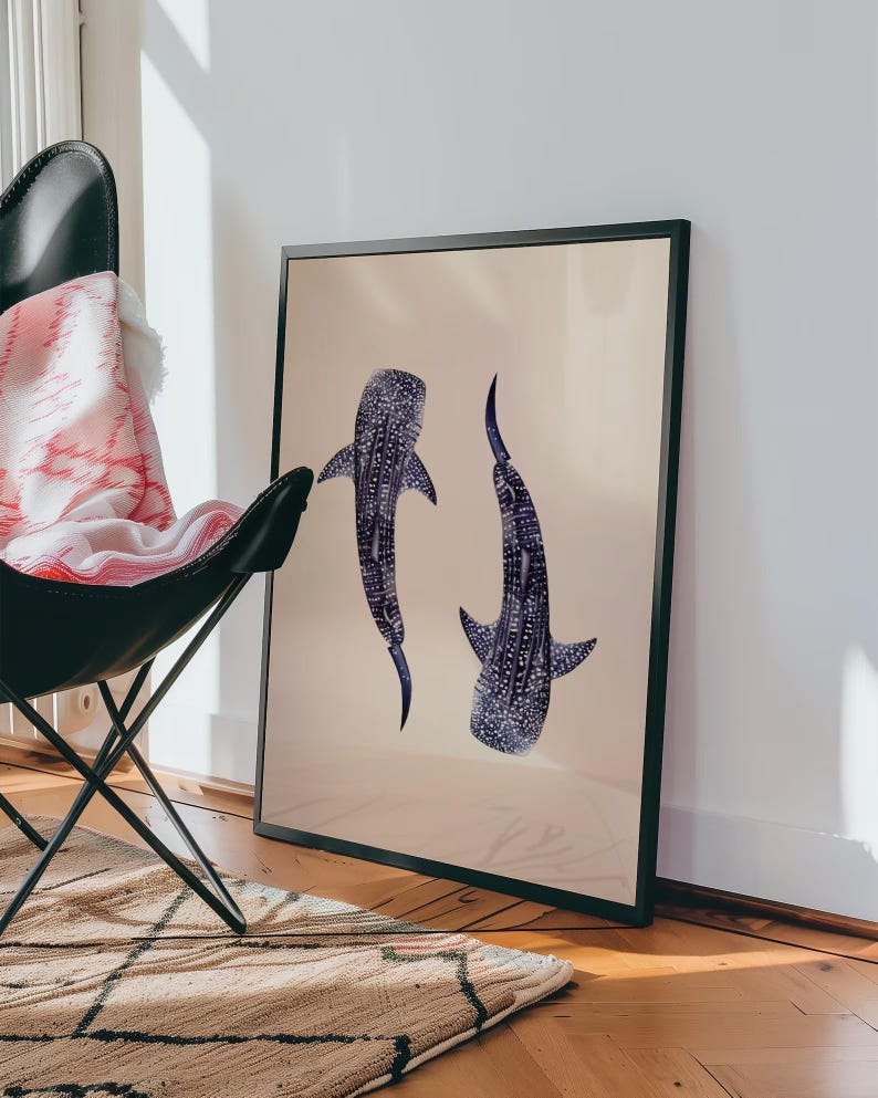 K&ouml;nnte beinhalten: Gerahmter Kunstdruck mit zwei stilisierten Walhaien in Blau- und Wei&szlig;t&ouml;nen vor beigem Hintergrund. Das Kunstwerk wird in einem schwarzen Rahmen pr&auml;sentiert und verleiht der Illustration mit maritimem Thema eine moderne Note.