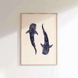 K&ouml;nnte beinhalten: Gerahmter Druck mit zwei Walhaien. Die Haie sind in Dunkelblau mit wei&szlig;en Punkten dargestellt, vor einem cremefarbenen Hintergrund. Das Kunstwerk ist in einem hellbraunen Holzrahmen gerahmt, f&uuml;r die Wanddekoration.