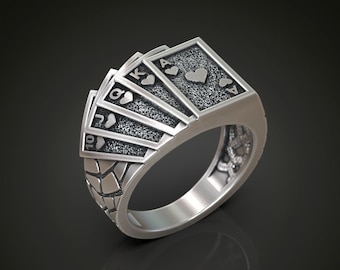Puede incluir: Un anillo de plata con un diseño de cartas de juego en forma de abanico. Las cartas son todas de corazones e incluyen el 10, la jota, la reina, el rey y el as.