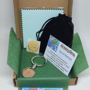 May include: A green and brown cardboard box with a green tissue paper lining. The box contains a silver keyring with a copper penny attached, a small black velvet bag, a blue polishing cloth, and a card with the text "Micheleys Shop Special Keyrings I hope that you'll love your keyring. To help maintain your penny there is a metal polishing cloth enclosed. The penny will tarnish over time and will move around which is completely natural." and a small sticker that says "handmade with love".