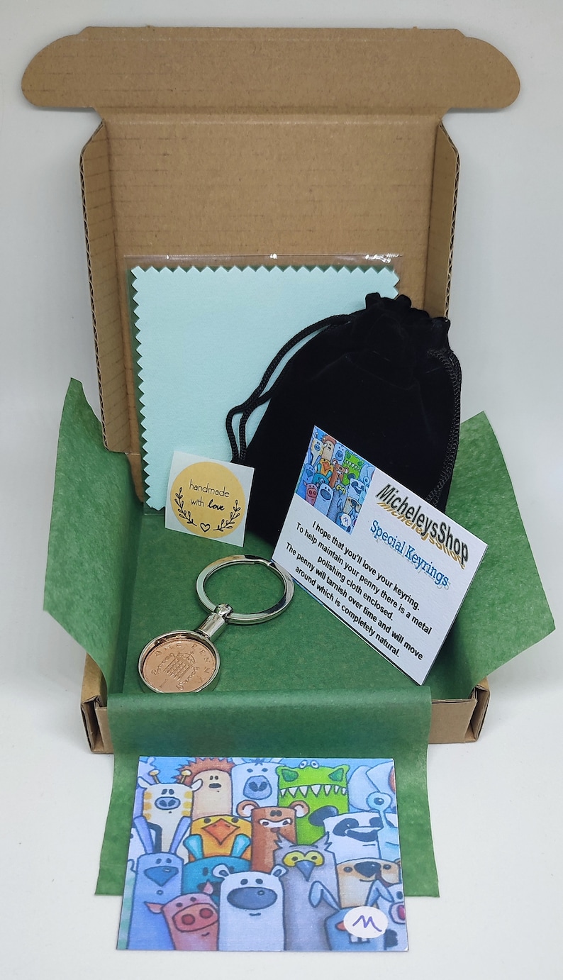 May include: A green and brown cardboard box with a green tissue paper lining. The box contains a silver keyring with a copper penny attached, a small black velvet bag, a blue polishing cloth, and a card with the text "Micheleys Shop Special Keyrings I hope that you'll love your keyring. To help maintain your penny there is a metal polishing cloth enclosed. The penny will tarnish over time and will move around which is completely natural." and a small sticker that says "handmade with love".