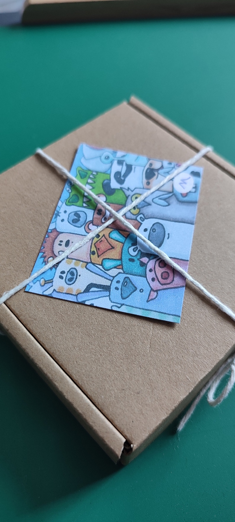 May include: A brown cardboard box with a white string tied around it. The box has a colorful sticker on it with a cartoon image of a group of animals. The sticker has the letter "M" written on it.
