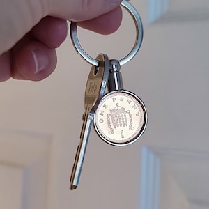 May include: A silver key ring with a Yale key and a British one penny coin attached. The coin features the image of the Houses of Parliament.