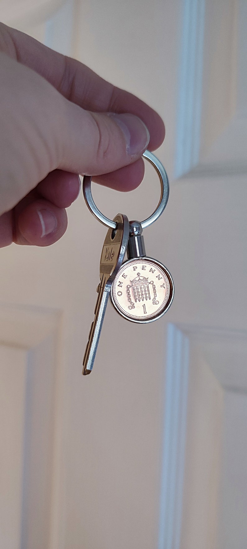 May include: A silver key ring with a Yale key and a British one penny coin attached. The coin features the image of the Houses of Parliament.