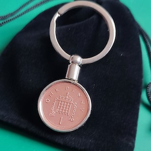 May include: A silver key chain with a one penny coin attached. The coin is copper colored and features the British coat of arms. The key chain is in a black velvet pouch.