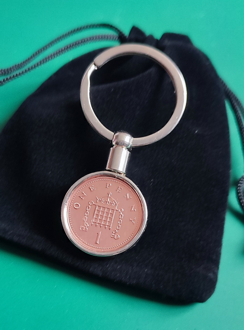 May include: A silver key chain with a one penny coin attached. The coin is copper colored and features the British coat of arms. The key chain is in a black velvet pouch.