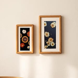 two framed pictures hanging on a white wall. The left frame contains a collage of various flowers, including daisies, roses, and lilies, arranged in a visually appealing manner. The right frame showcases a close-up of a flower, highlighting its intricate details and vibrant colors.