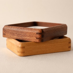 May include: Two rectangular wooden trays stacked on top of each other. The top tray is made of dark brown wood, while the bottom tray is made of light tan wood. Both trays feature visible finger joint construction at the rounded corners.